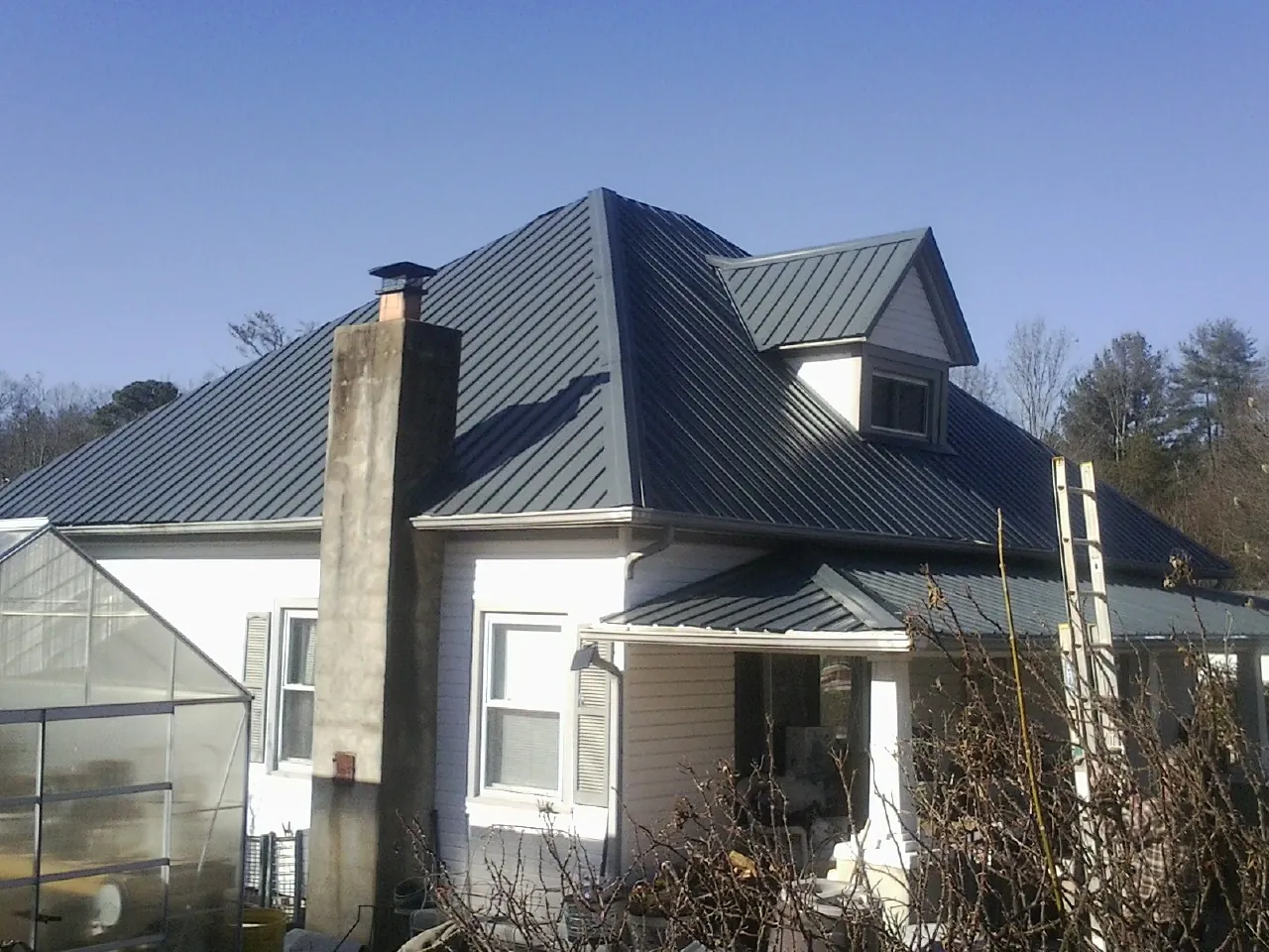 Dark blue standing seam metal roof on a white farmhouse with dormer — Slate & Tile Roof Repair by Roofing Brothers in Mount Airy