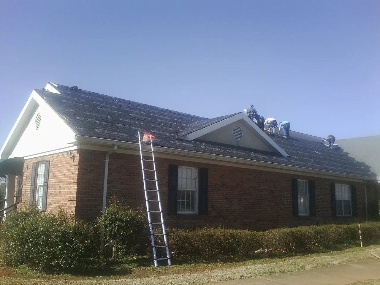 Crew tearing shingles off a brick ranch roof with a ladder set — Emergency Roof Repair work by our crew in Mount Airy