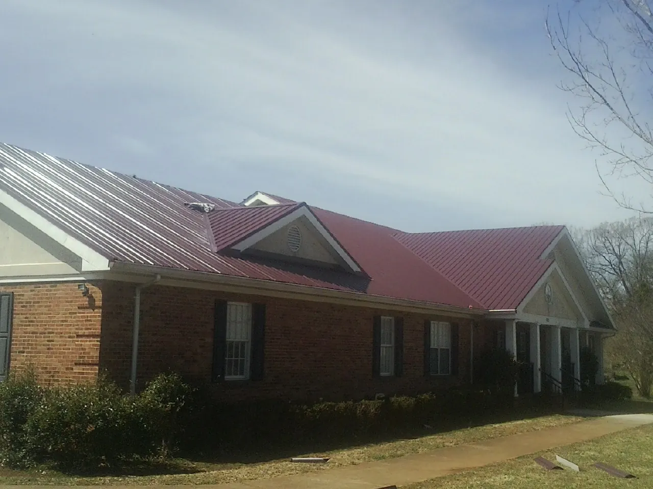 Red metal roof with gabled entries on a long brick building, from a Hail Damage Roof Repair job in Mount Airy