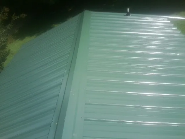New green metal panels meeting at the ridge of a roof — Flat Roof Repair work by our crew in Mount Airy