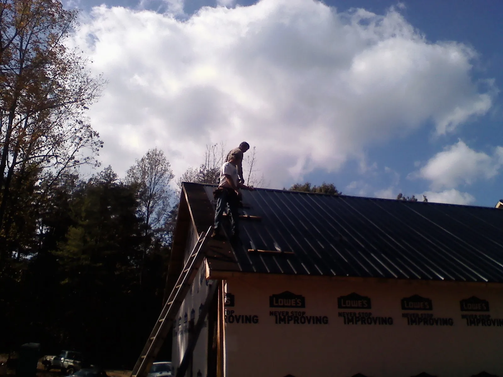 Roofer fastening dark metal panels high against a cloudy sky, from a Roof Inspection job in Mount Airy
