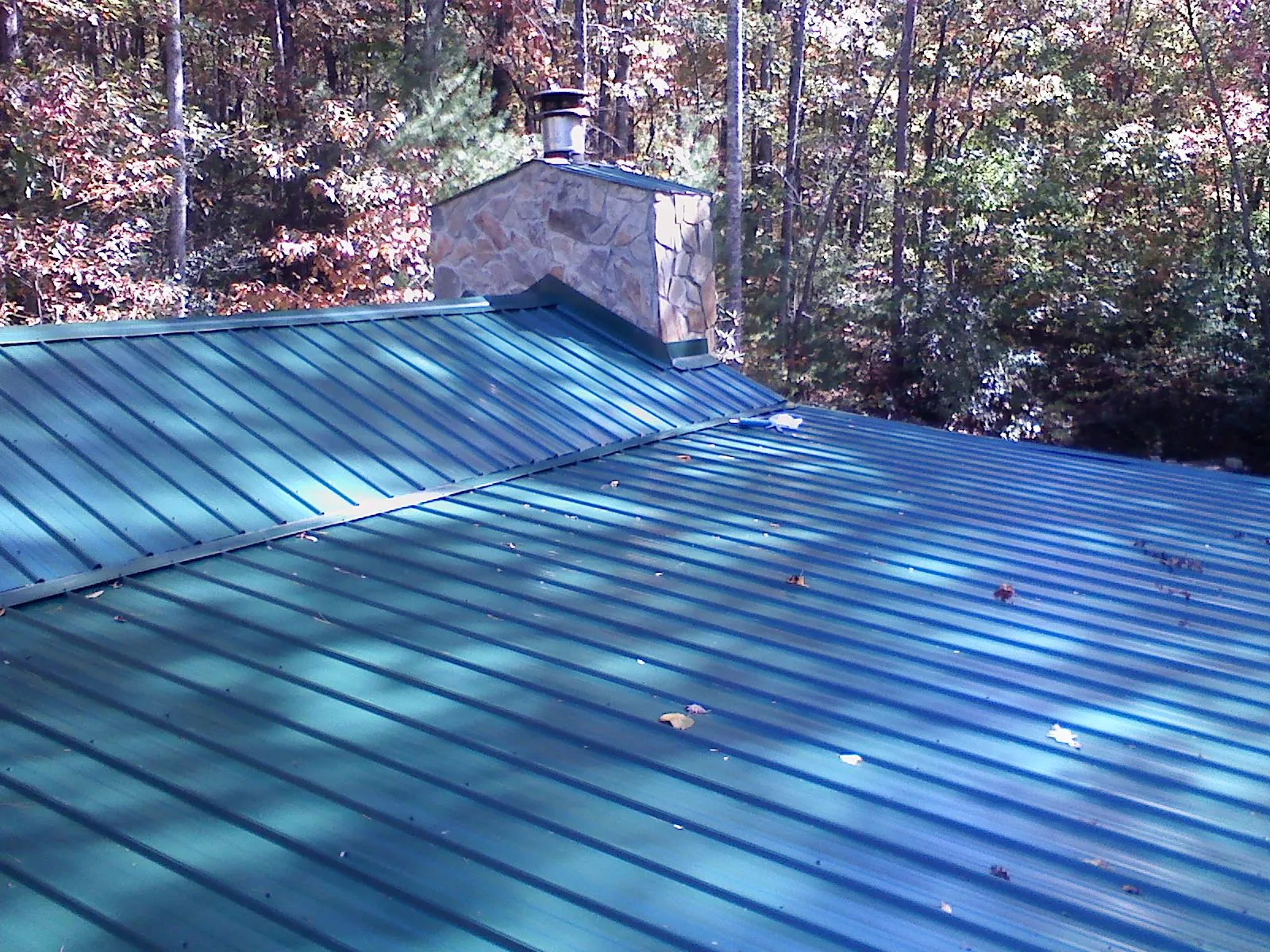 New green metal roof and stone chimney surrounded by autumn woods in Mount Airy