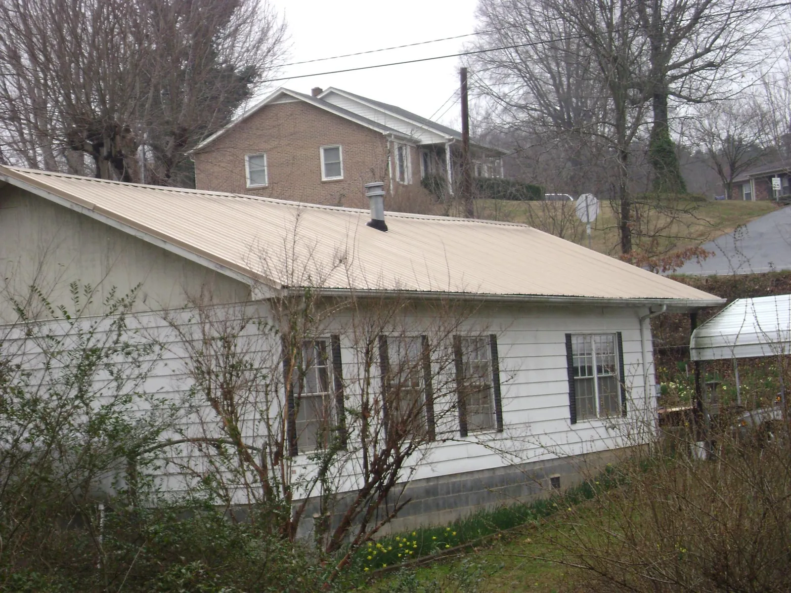 Tan metal roof on a white sided house set into a hillside — Commercial Roofing by Roofing Brothers in Mount Airy