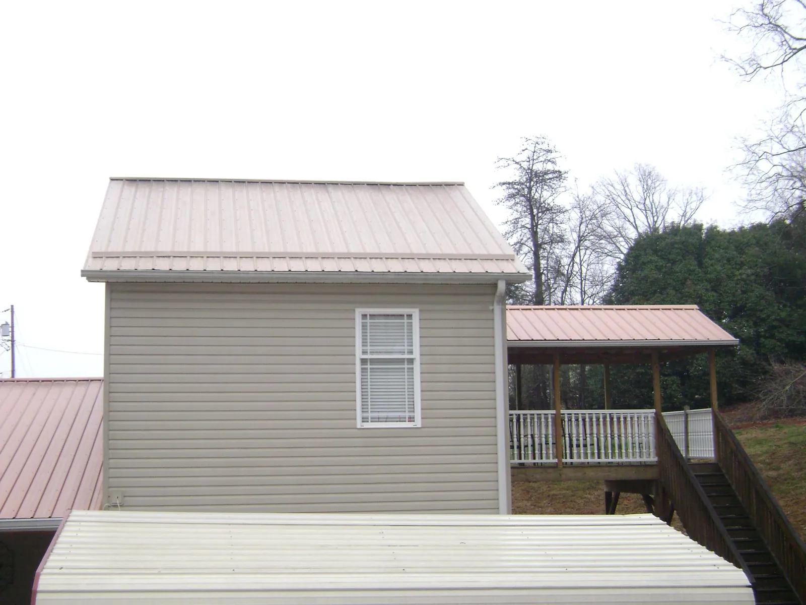 Tan metal roofs on a two story addition and attached porch, from a Roof Replacement job in Mount Airy